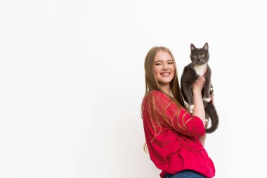 Mutlu genç bir kadın kucağında kabarık bir kedi ve beyaz bir kameraya bakıyor. 