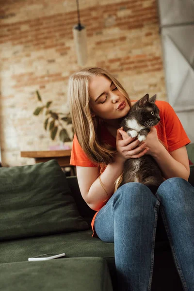 迷人的年轻女子抱着可爱的猫靠近沙发上的智能手机 — 图库照片