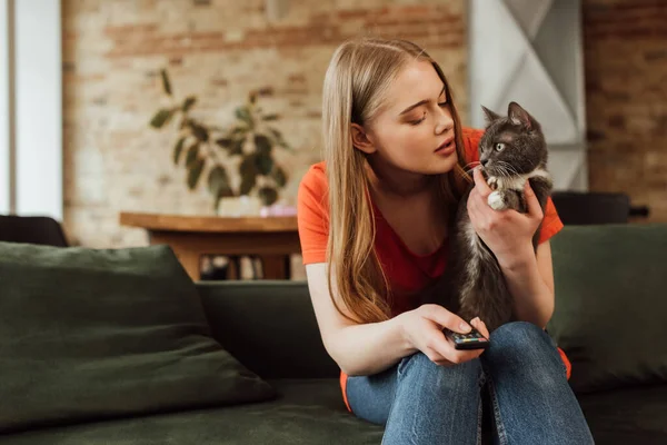 リモコンを持って可愛い猫を見る若い女性 — ストック写真