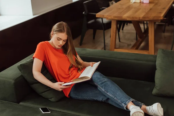 Beautiful Girl Reading Book Smartphone Blank Screen Living Room — Stock Photo, Image