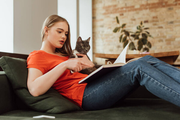 selective focus of beautiful woman holding cat and reading book in living room 