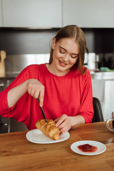 happy girl holding knife and cutting tasty croissant on plate