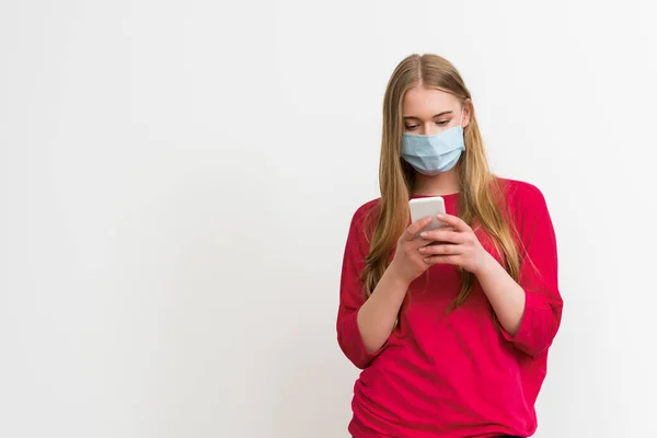 戴医疗面具 手持智能手机 被白色隔离的年轻女子 — 图库照片