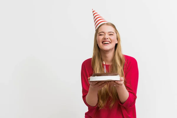 明るい女の子でパーティーキャップ笑顔とホワイトに隔離された誕生日ケーキを保持 — ストック写真