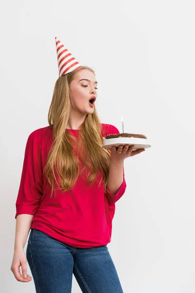 在生日蛋糕上吹灭蜡烛的戴著派对帽的女孩被白色隔离了 — 图库照片