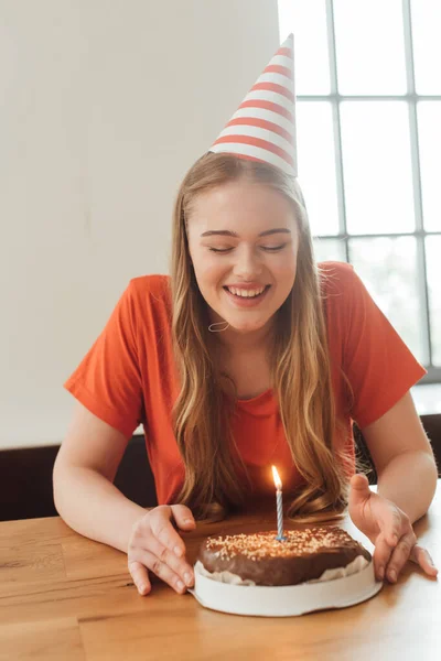 cheerful woman in party cap looking at delicious birthday cake