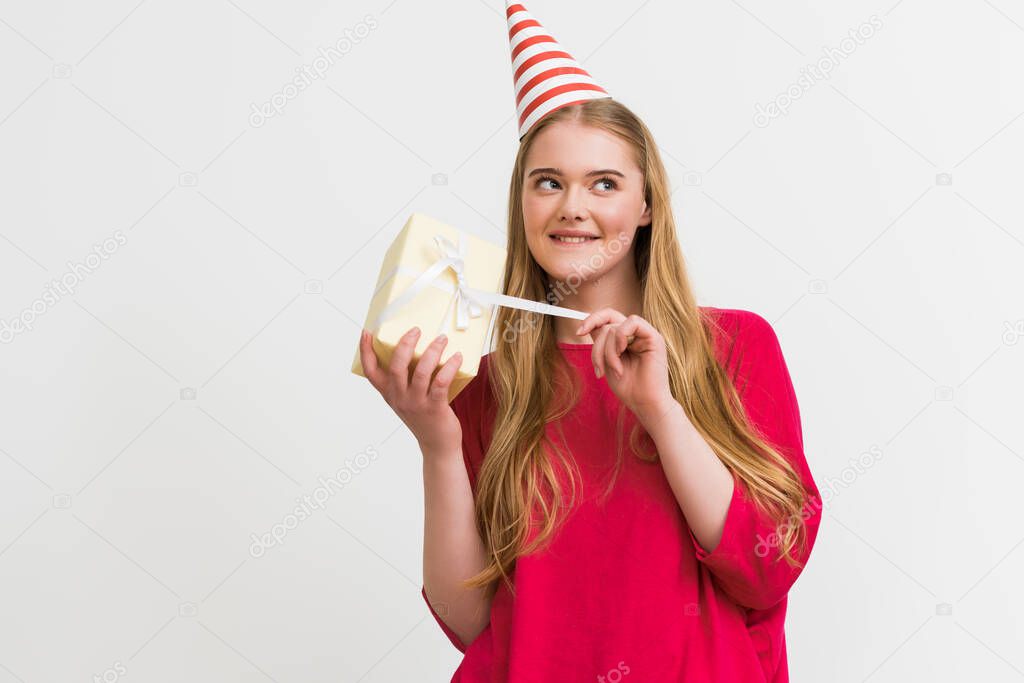 curious girl in party cap touching ribbon on present isolated on white 