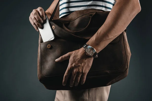 Мужчина кладет смартфон в сумку — стоковое фото