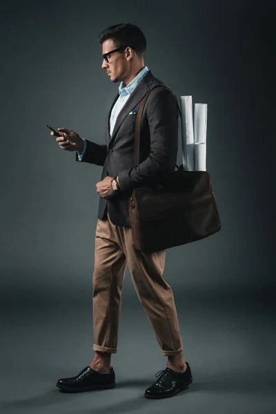 Businessman with blueprints in bag using smartphone — Stock Photo