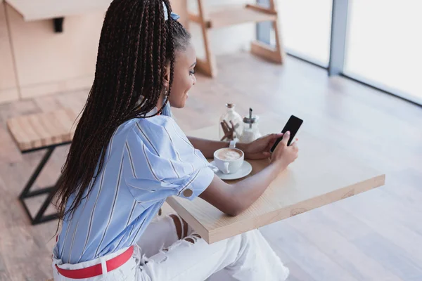 Femme afro-américaine utilisant un smartphone dans un café — Photo de stock
