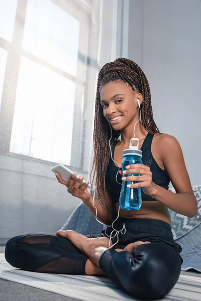 Mujer deportiva con teléfono inteligente y botella de agua - foto de stock