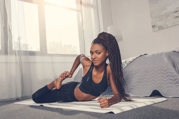 Mujer estirando pierna en esterilla de yoga - foto de stock