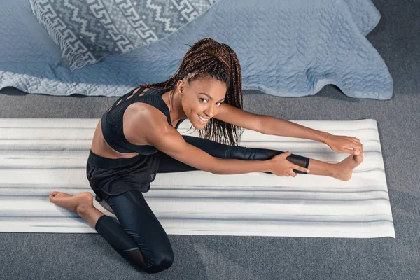 Mujer estirando pierna en esterilla de yoga - foto de stock
