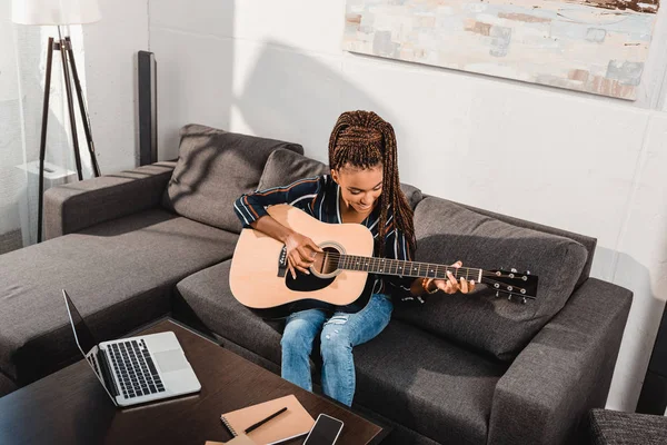 Woman playing guitar on couch — Stock Photo