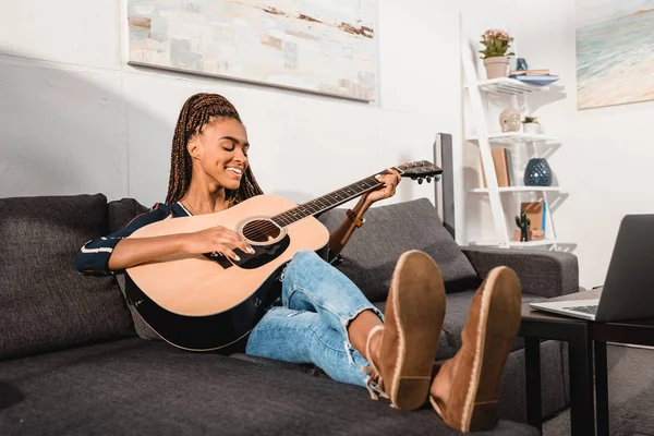 Mujer tocando guitarra en el sofá - foto de stock