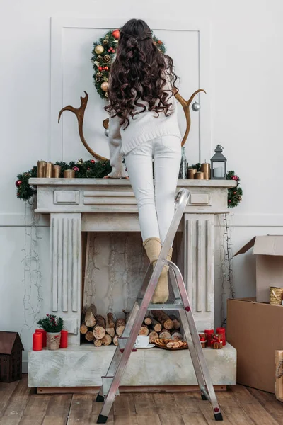 Woman hanging christmas wreath over fireplace — Stock Photo