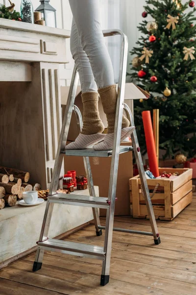 Frau schmückt Raum für Weihnachten auf Leiter — Stockfoto