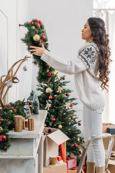 Woman hanging christmas wreath over fireplace — Stock Photo