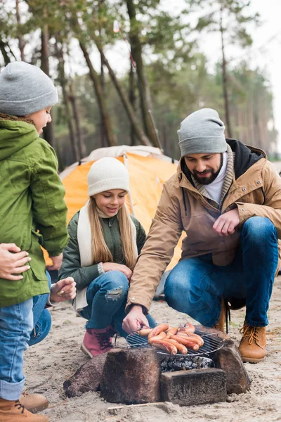 Father and kids grilling sausages on nature — Stock Photo