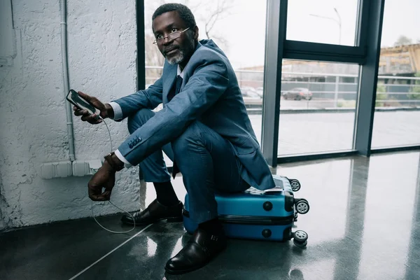 Hombre de negocios esperando carga de teléfonos inteligentes en el aeropuerto - foto de stock