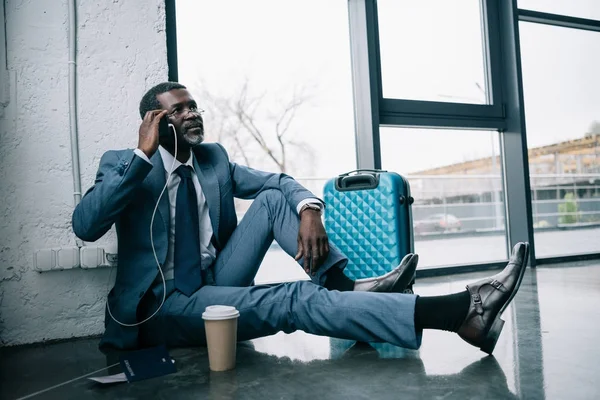 Hombre de negocios sentado en el suelo y hablando por teléfono inteligente - foto de stock