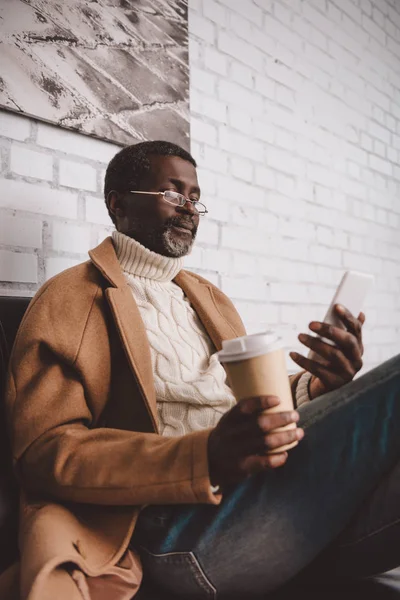 Hombre sosteniendo café y mirando el teléfono inteligente - foto de stock