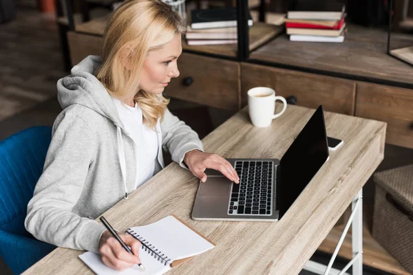 Mujer tomando notas y utilizando el ordenador portátil - foto de stock