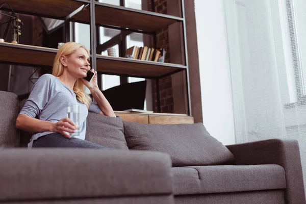 Woman drinking water and talking on smartphone — Stock Photo