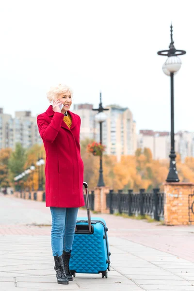 Mujer mayor con maleta y teléfono inteligente - foto de stock