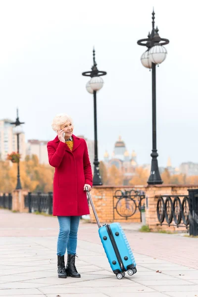 Пожилая женщина с чемоданом и смартфоном — стоковое фото