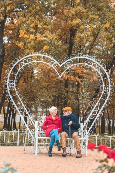 Couple aîné sur banc en forme de coeur — Photo de stock