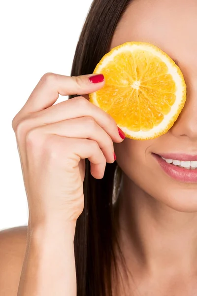 Mujer cubriendo el ojo con rebanada de naranja - foto de stock