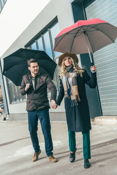 Stylish young couple with umbrellas — Stock Photo