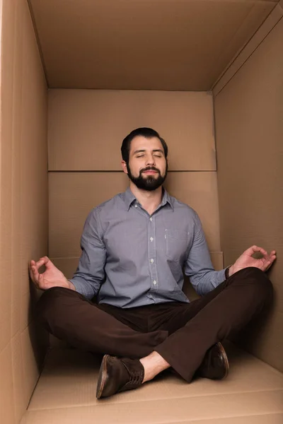 Homme méditant dans une boîte en carton — Photo de stock