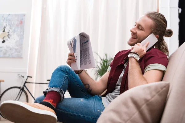 Schöner Mann liest Zeitung und telefoniert zu Hause mit dem Smartphone — Stockfoto