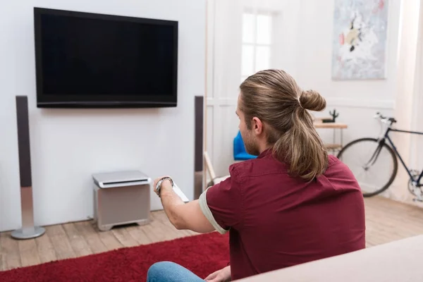 Vista trasera del hombre con control remoto ver la televisión en casa - foto de stock