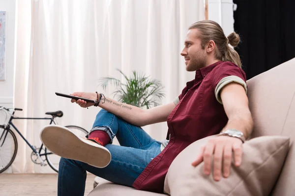 Homem bonito com controle remoto assistindo tv em casa — Fotografia de Stock