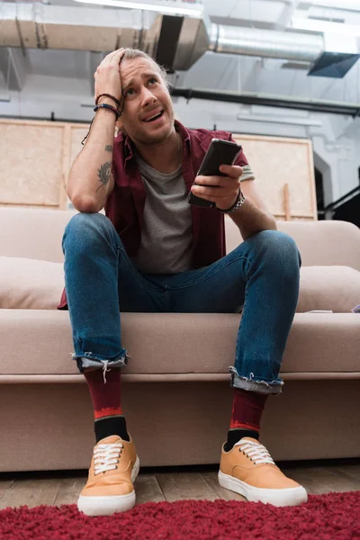 Chateado homem bonito com controle remoto assistindo tv em casa — Fotografia de Stock