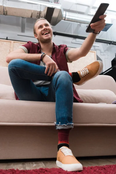 Excité bel homme avec télécommande regarder la télévision à la maison — Photo de stock