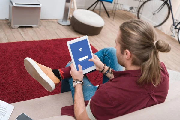 Hombre sentado en el sofá, mientras que el uso de tableta digital con aparato de facebook - foto de stock