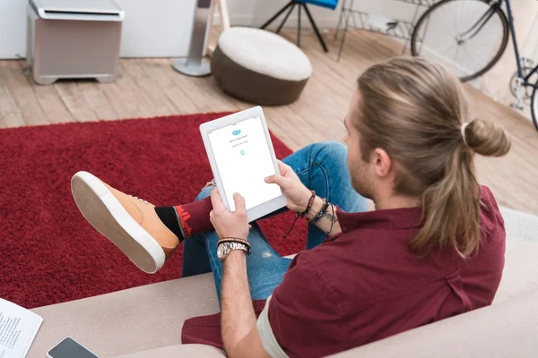 Mann sitzt auf Sofa und nutzt digitales Tablet mit Skype-Gerät — Stockfoto