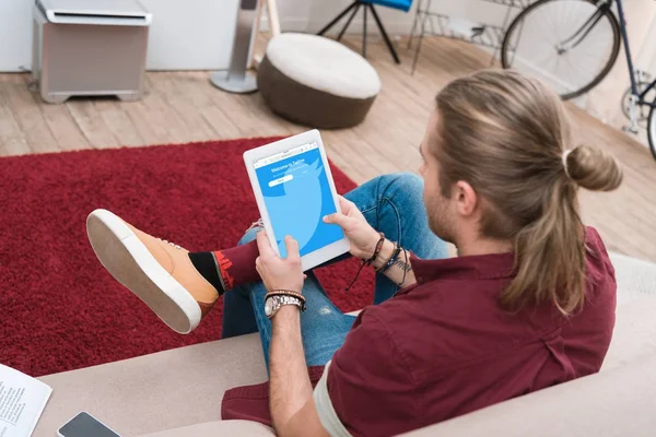 Mann sitzt auf Sofa und nutzt digitales Tablet mit Twitter-Gerät — Stockfoto