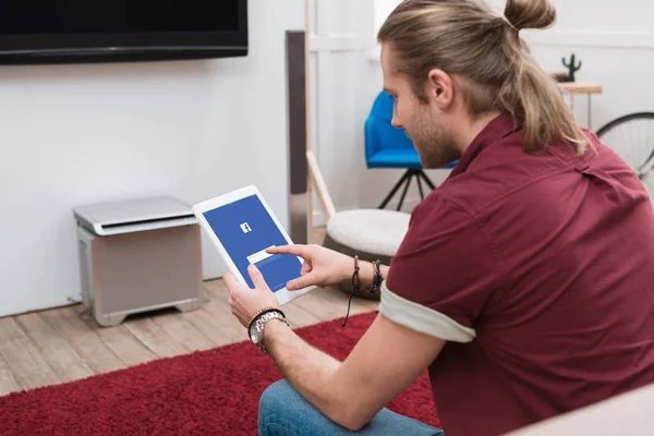 Homme assis sur le canapé tout en utilisant une tablette numérique avec appareil facebook — Photo de stock