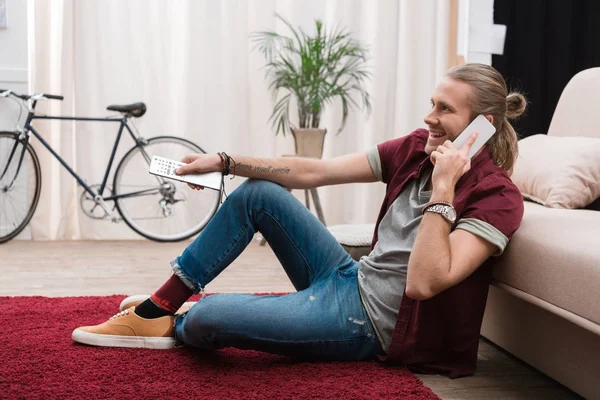 Schöner Mann, der auf dem Smartphone spricht, während er zu Hause fernsieht — Stockfoto