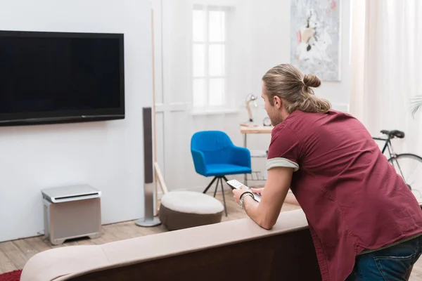 Homem com controle remoto assistindo TV em casa — Fotografia de Stock