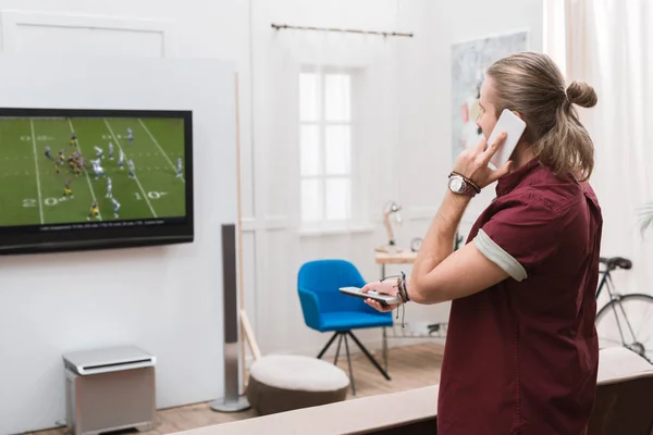 Mann telefoniert auf Smartphone, während er Fußballspiel zu Hause anschaut — Stockfoto