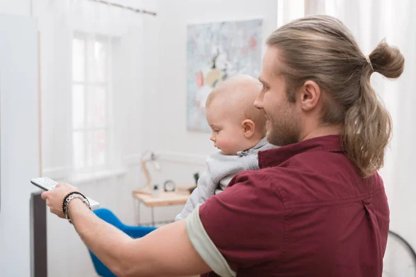 Smiling father watching TV with little baby boy at home — Stock Photo