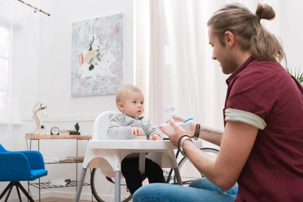 Padre nutrire il suo piccolo figlio con il cibo per bambini a casa — Foto stock