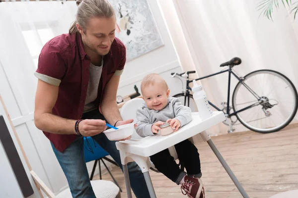 Padre felice che nutre suo figlio sorridente con il cibo per bambini a casa — Foto stock