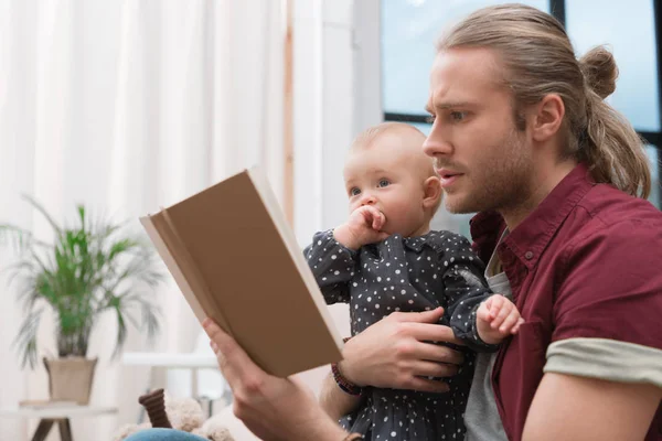 Отец читает книгу маленькой дочери дома — стоковое фото